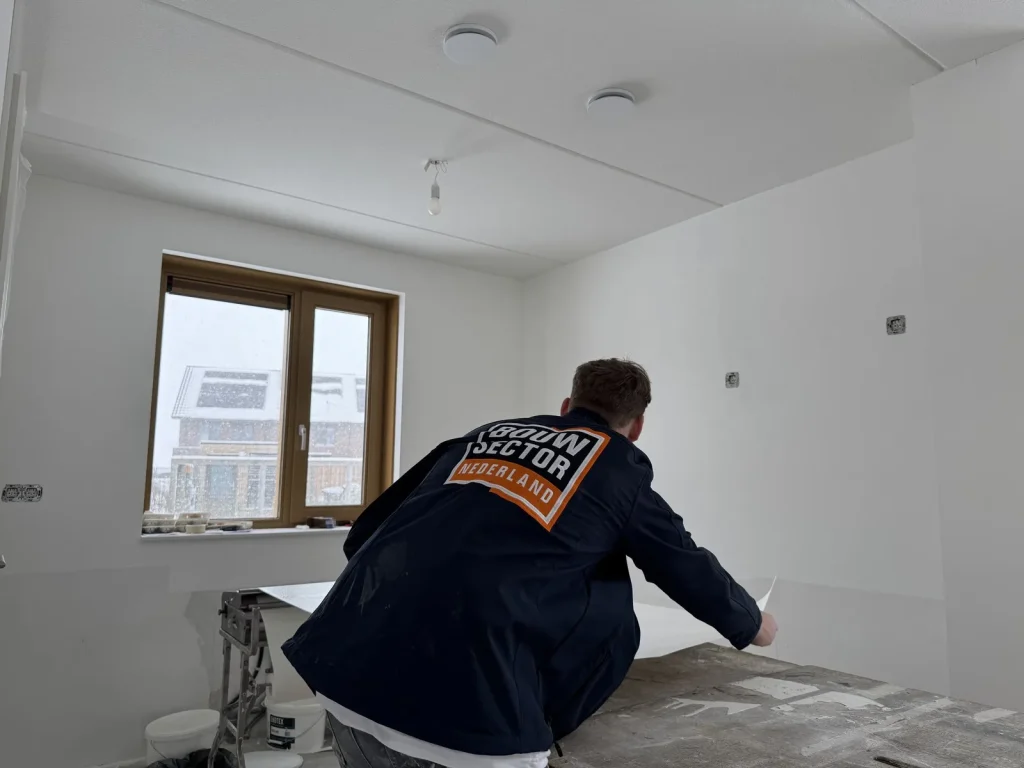 Behanger van Bouwsector Nederland in donkere werkjas legt een baan op de plaktafel bij een raam met sneeuw buiten