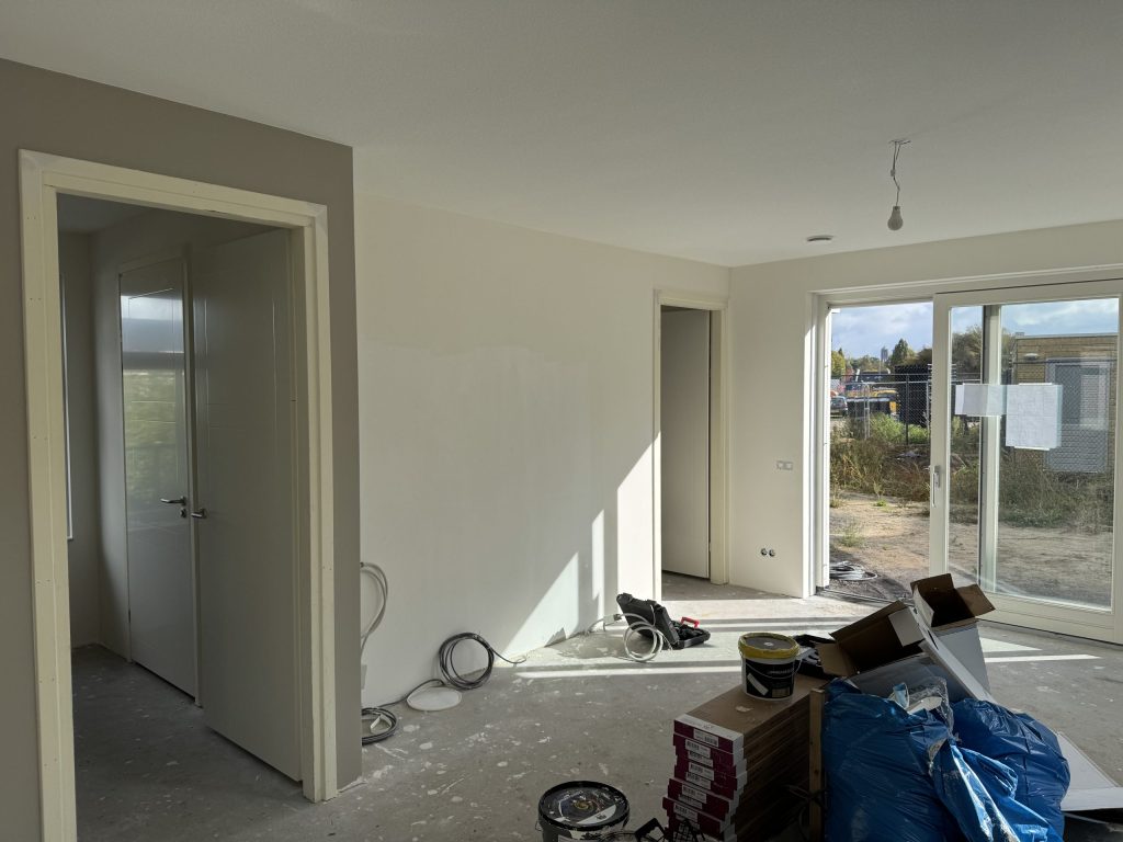 Nieuwbouwwoning tijdens de afwerking met verfemmers, pakken laminaat en een schuifpui naar de bouwplaats
