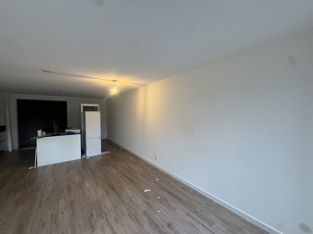Lange lichte wand in een woonkamer met keukenblok en laminaatvloer, net afgewerkt