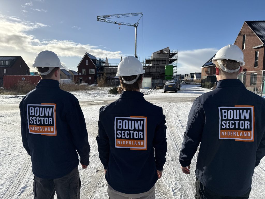 Drie medewerkers van Bouwsector Nederland met witte helm op een besneeuwde bouwplaats met nieuwe huizen en een bouwkraan